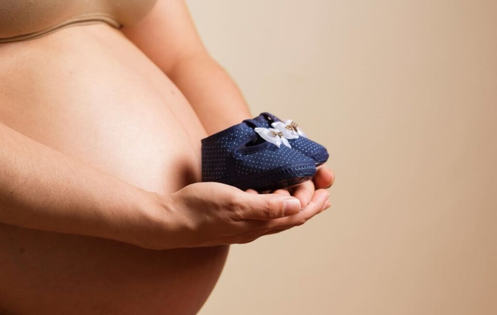 Femme enceinte tenant une paire de chaussons de bébé